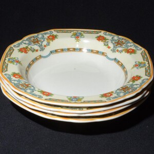 May include: A set of three white ceramic soup bowls with a floral pattern in shades of orange, blue, and green. The bowls have a scalloped edge and a gold trim.