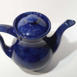 May include: A cobalt blue ceramic teapot with a rounded body and a curved spout. The teapot has a lid with a knob on top.