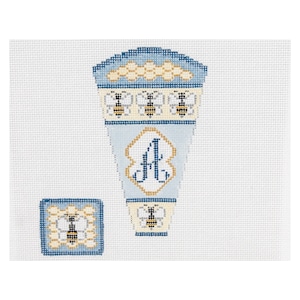 May include: A blue and white needlepoint canvas with a beehive design and the letter "A" monogrammed in the center. The beehive is surrounded by bees.