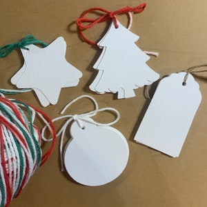 May include: Five white paper gift tags shaped like a star, a Christmas tree, a circle, and two rectangular tags. The tags have holes punched in the top and are tied with twine.