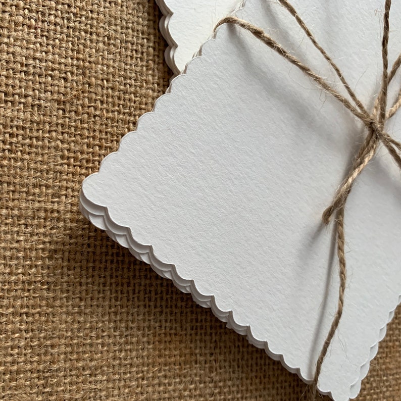 May include: A stack of white, scalloped edge cards tied together with twine. The cards are on a brown burlap background.