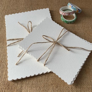 May include: Two white cards with scalloped edges are tied together with twine. The cards are stacked on top of each other and the twine is tied in a bow.