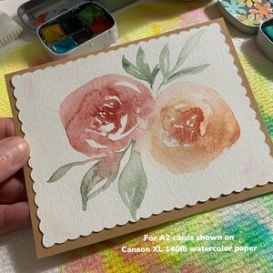 May include: A watercolor painting of two pink and orange flowers with green leaves on a white card. The card is on a brown background with the text "For A2 cards shown on Canson XL 140lb watercolor paper".