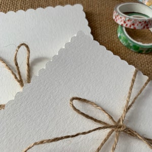 May include: Two white scalloped cards tied together with twine. The twine is tied in a bow on the front of the cards.