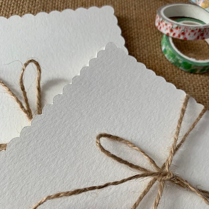 May include: Two white scalloped cards tied together with twine. The twine is tied in a bow on the front of the cards.