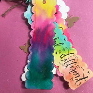 May include: Set of four colorful watercolor bookmarks with scalloped edges. Each bookmark features a different watercolor design and the text "Be to different" in black calligraphy.