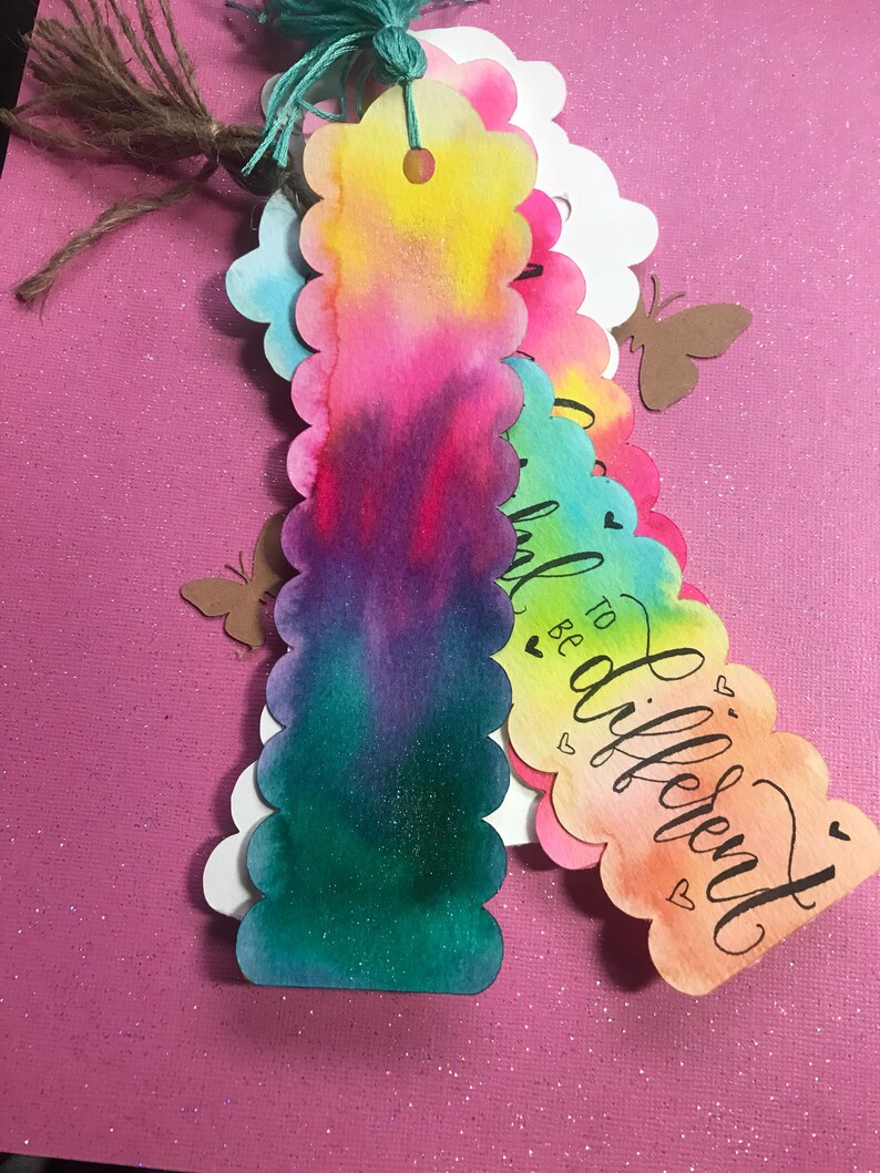 May include: Set of four colorful watercolor bookmarks with scalloped edges. Each bookmark features a different watercolor design and the text "Be to different" in black calligraphy.