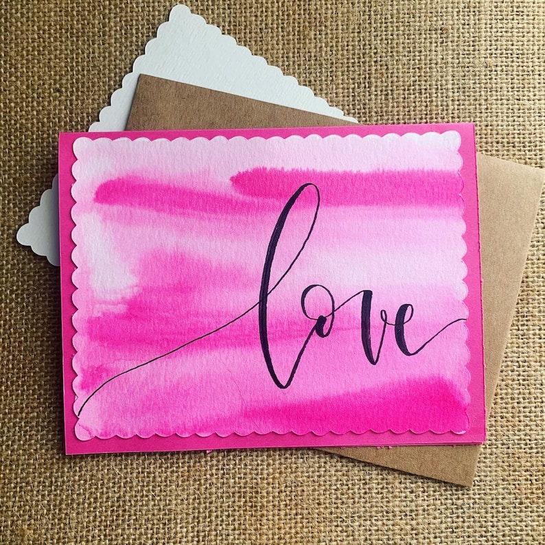 May include: Pink watercolor card with a scalloped edge and the word "love" written in black calligraphy.