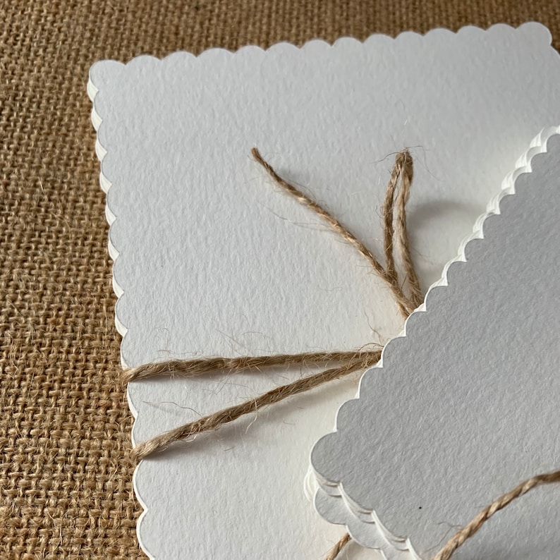 May include: A stack of white scalloped edge cards tied together with twine.
