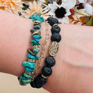 May include: Three bracelets are displayed. One features turquoise stones with gold accents. Another has black lava beads and a gold leaf charm. A third bracelet is a delicate gold chain. The bracelets are stacked together.
