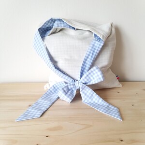Puede incluir: Una bolsa de lino con una cinta de cuadros vichy azul claro y blanco atada con un lazo. El interior y el ribete de la bolsa presentan el mismo patrón de cuadros. La bolsa está sobre una superficie de madera.