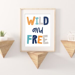 May include: A framed print with the text "WILD and FREE" in colorful letters with a geometric pattern. The print is on a white background and is framed in a light wood frame.