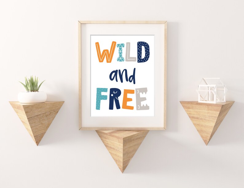 May include: A framed print with the text "WILD and FREE" in colorful letters with a geometric pattern. The print is on a white background and is framed in a light wood frame.