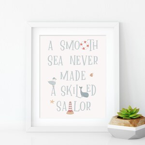 May include: A white framed print with a light pink background and blue text that reads "A smooth sea never made a skilled sailor". The print features nautical illustrations including a seagull, a whale, a life preserver, a starfish, and a lighthouse.