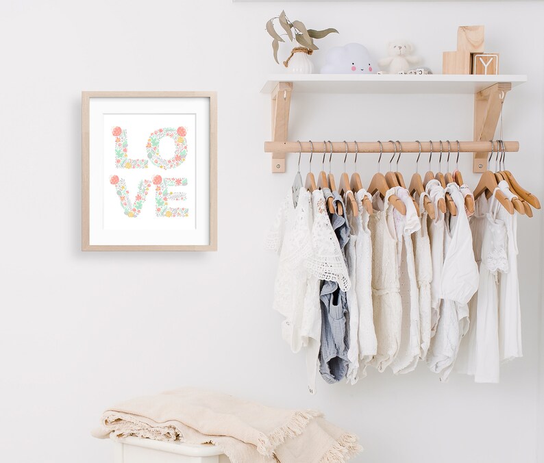 May include: A framed print with the word "LOVE" spelled out in floral letters. The letters are made up of pink, green, and yellow flowers. The print is hanging on a white wall above a wooden shelf with a white cloud-shaped nightlight and wooden blocks.