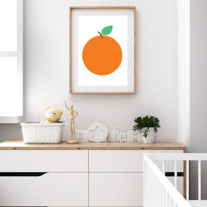 Puede incluir: Una impresi&oacute;n enmarcada de una naranja simple con una hoja verde sobre un fondo blanco. La impresi&oacute;n est&aacute; colgada en una pared blanca sobre una c&oacute;moda blanca con una tapa de madera. Hay un oso de peluche, una mu&ntilde;eca de madera, una estrella blanca y un letrero de madera que dice "Hola" en la c&oacute;moda.