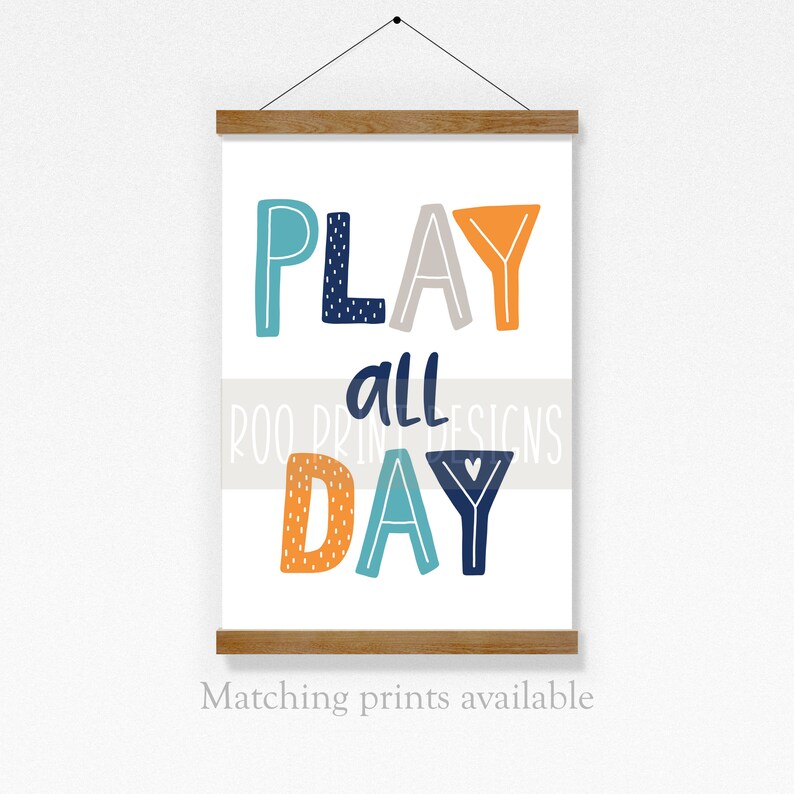May include: A white canvas print with the text "PLAY all DAY" in colorful, stylized letters. The letters are in shades of blue, orange, and gray. The text "Roo Print Designs" is in smaller letters below the main text.