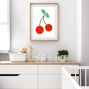 May include: A framed print of a red cherry with a green stem and leaves on a white background. The print is hanging on a white wall above a white dresser with drawers.