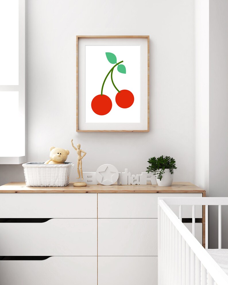 May include: A framed print of a red cherry with a green stem and leaves on a white background. The print is hanging on a white wall above a white dresser with drawers.