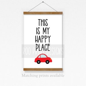 May include: A white printable wall art sign with black text that reads "This is my happy place" and a red car illustration. The sign is framed with a wooden frame.