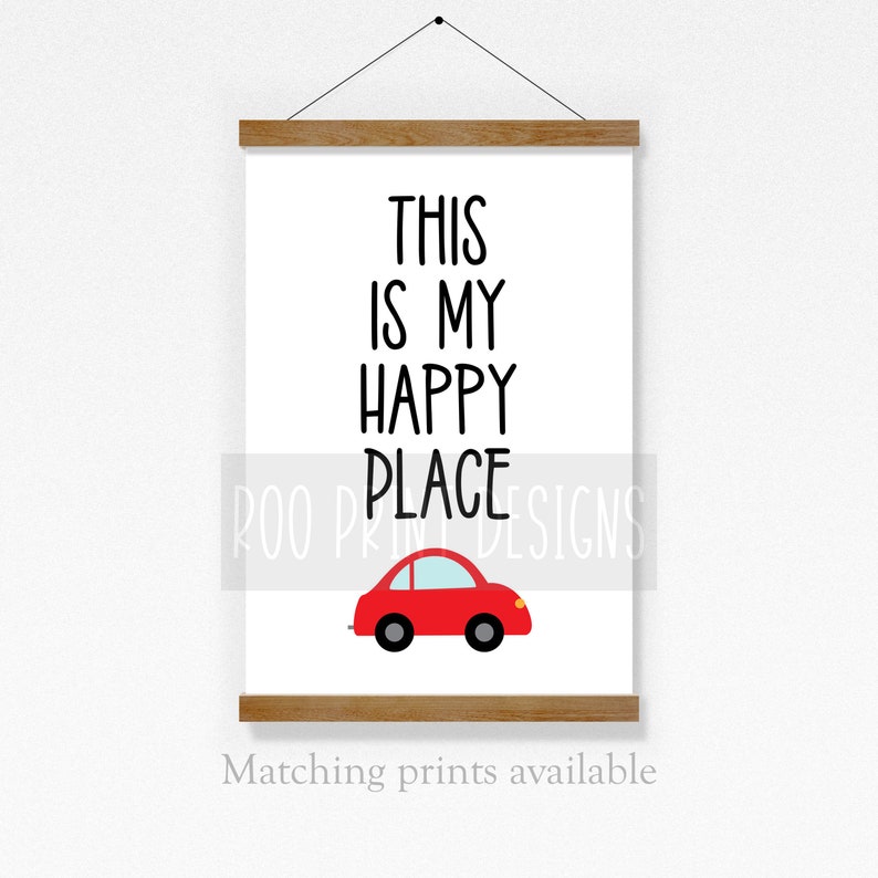May include: A white printable wall art sign with black text that reads "This is my happy place" and a red car illustration. The sign is framed with a wooden frame.
