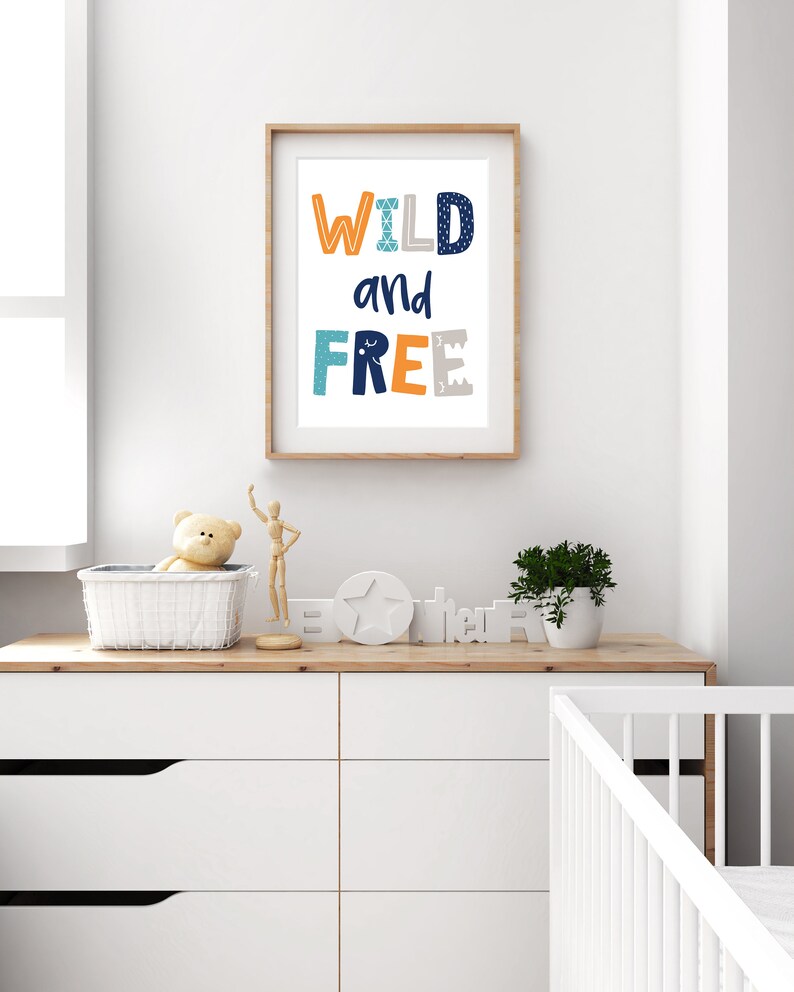 May include: A framed print with the text "WILD and FREE" in blue, orange, and gray letters. The letters have a geometric pattern and are set against a white background.