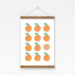 May include: A white framed print with a pattern of 12 orange oranges with green leaves and one orange slice. The oranges are arranged in a grid pattern.