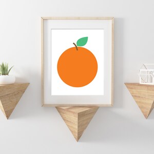 Puede incluir: Una impresi&oacute;n enmarcada de una naranja simple con una hoja verde sobre un fondo blanco. La impresi&oacute;n est&aacute; colgada en una pared blanca con dos estantes de madera triangulares.