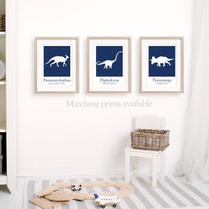 May include: Three framed prints with white dinosaur silhouettes on a navy blue background. The dinosaurs are labeled Parasaurolophus,  Diplodocus, and Triceratops. The text "Matching prints available" is below the prints.
