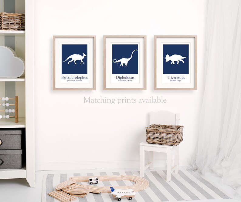 May include: Three framed prints with white dinosaur silhouettes on a navy blue background. The dinosaurs are labeled Parasaurolophus,  Diplodocus, and Triceratops. The text "Matching prints available" is below the prints.