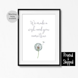 Op de afbeelding: Een witte ingelijste print met een grijze paardenbloem en de tekst "We made a wish and you came true".