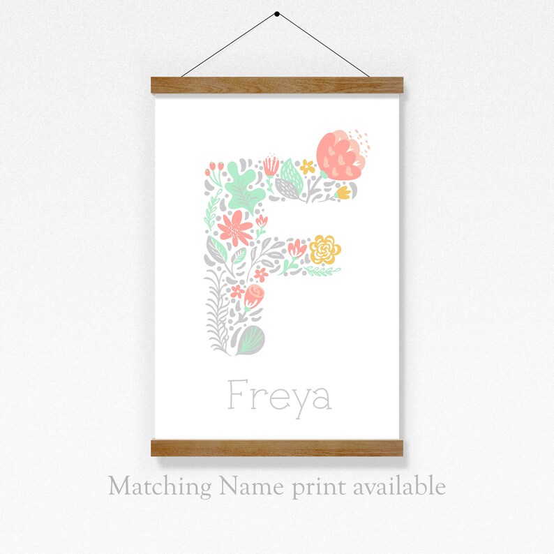 May include: A printable wall art design featuring the letter F made of flowers in shades of pink, green, and yellow. The name Freya is written below the letter. The design is on a white background and is framed with a wooden frame.