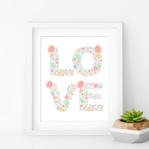 May include: A white framed print with the word "LOVE" spelled out in pastel pink, green, and gray floral designs.