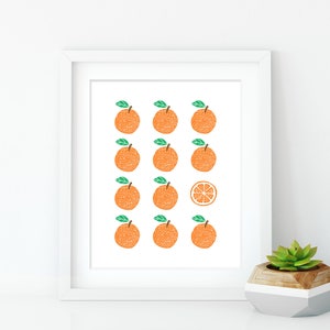 May include: A white framed print with a pattern of 12 orange fruits, all but one are whole, the last one is a slice of orange. The print is on a white background.