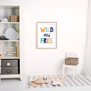 May include: A white framed print with the text "WILD and FREE" in colorful letters on a white wall in a nursery. The print is above a white wooden chair with a wicker basket.