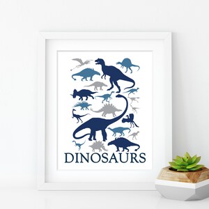May include: A white framed print with a blue and gray silhouette of various dinosaurs. The print has the word "DINOSAURS" at the bottom.