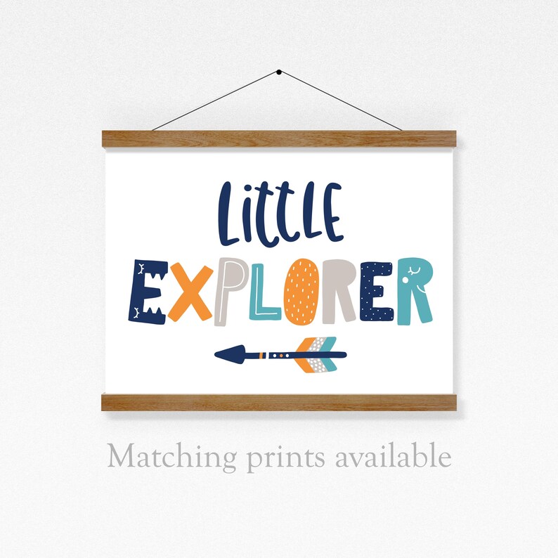 May include: A white canvas print with a wooden frame. The print features the text "Little Explorer" in colorful letters with a stylized arrow underneath. The text is in a blue, orange, and gray color scheme.