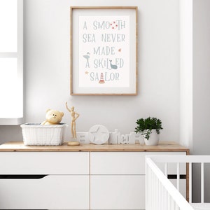 May include: A framed nursery print with a light blue background and white text that reads "A smooth sea never made a skilled sailor". The text is surrounded by small nautical illustrations in red, blue, and gray.