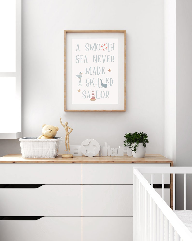 May include: A framed nursery print with a light blue background and white text that reads "A smooth sea never made a skilled sailor". The text is surrounded by small nautical illustrations in red, blue, and gray.