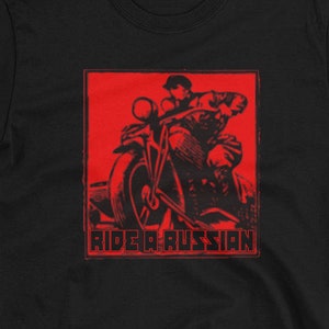 May include: Black t-shirt featuring a red graphic of a person riding a motorcycle with the text "Ride a Russian" in red.