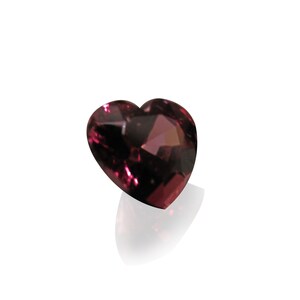 May include: A heart-shaped, deep pink gemstone with facets.