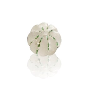 May include: A white glass bead with green lines, resembling a small pumpkin.