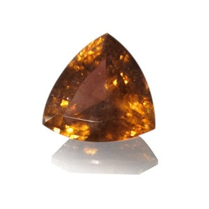May include: A triangular, faceted gemstone with a golden brown color. The gemstone has a translucent appearance with a slight shimmer.