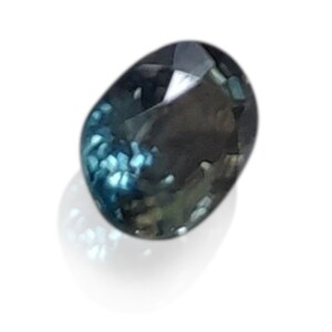 May include: An oval-shaped gemstone in shades of dark blue with a light blue and green shimmer.
