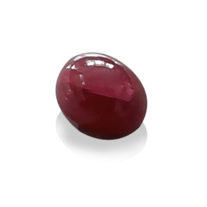 May include: A polished, oval-shaped gemstone with a deep red hue. The gem has a smooth, reflective surface, and is set against a white background. The gemstone appears to be a cabochon, a style often used in jewelry.