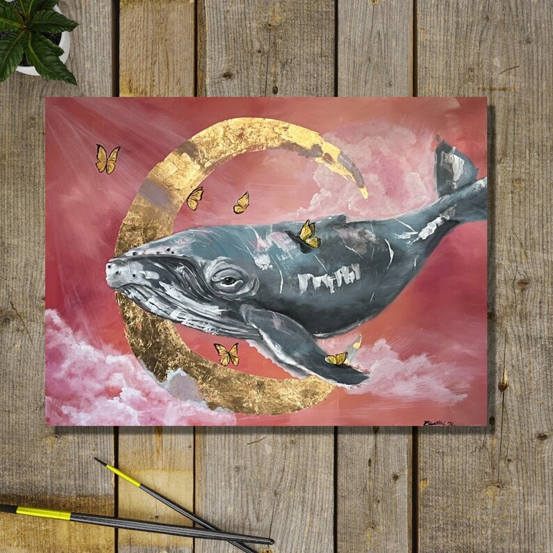 May include: A painting of a whale swimming through a pink and gold sky with a crescent moon. The whale is gray and white, and the sky is filled with small yellow butterflies.
