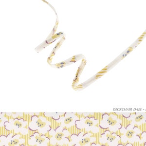 Puede incluir: Una cinta blanca con un patrón floral amarillo y azul. La cinta está enroscada y retorcida. El texto "DECKCHAIR DAZE - B" es visible en la parte inferior de la imagen.