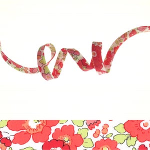 May include: A pink and green floral ribbon with a white background. The ribbon is curled and twisted.