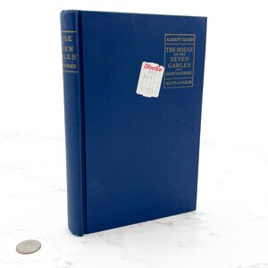 May include: A hardcover book titled "The House of the Seven Gables" by Hawthorne. The book has a dark blue cover with gold lettering and a white price tag. The book is part of the Academy Classics series.