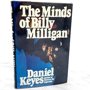 May include: A hardcover book titled "The Minds of Billy Milligan" by Daniel Keyes. The cover features a dark blue background with white text and a portrait of multiple faces. The author's name and the title of another book are also visible.